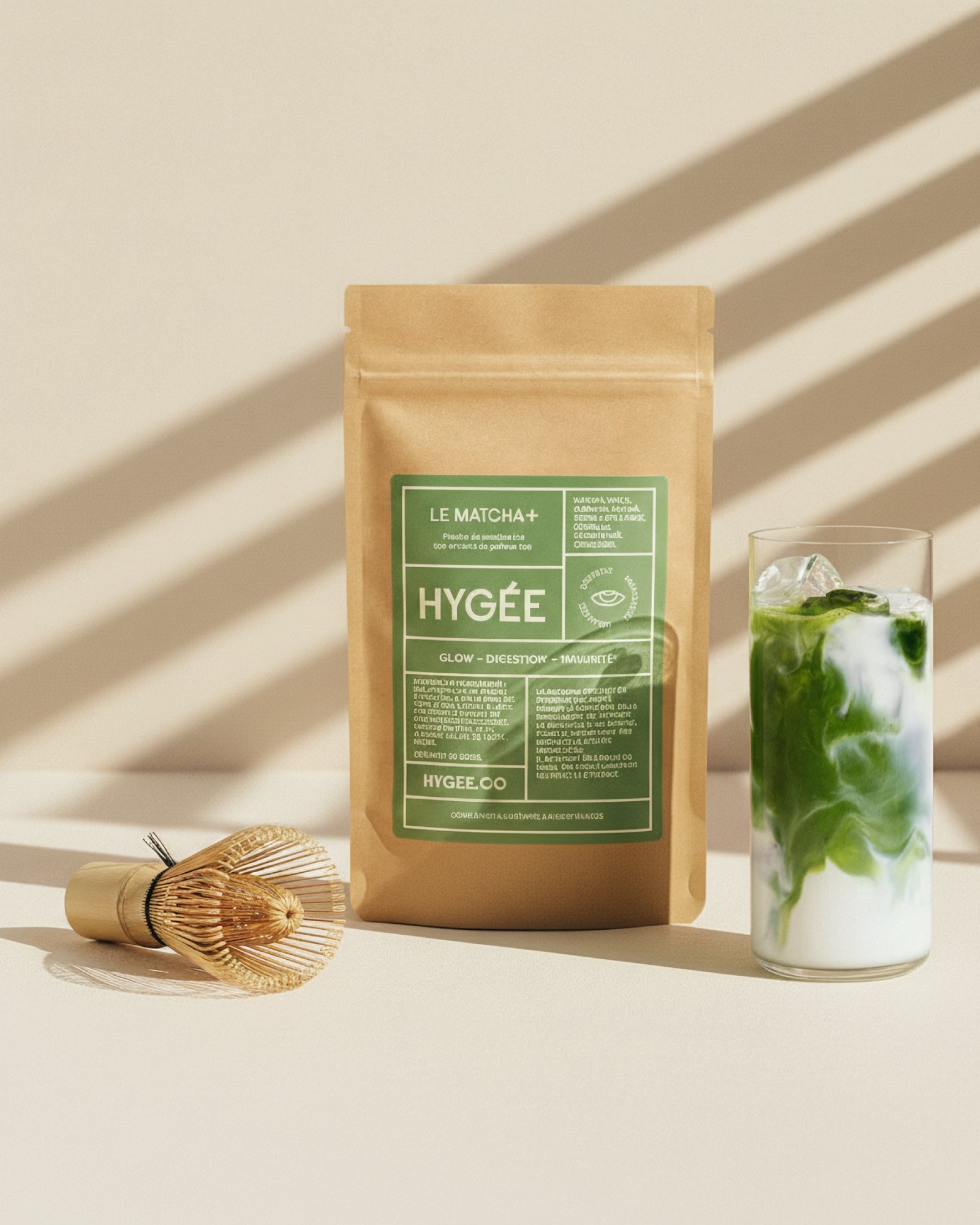 A kraft pouch of Allnord’s HYGÉE Le Matcha+ stands beside a bamboo whisk and a layered iced matcha on a sunlit surface with striped shadows. A clean studio composition with calm neutrals and fresh green swirls.