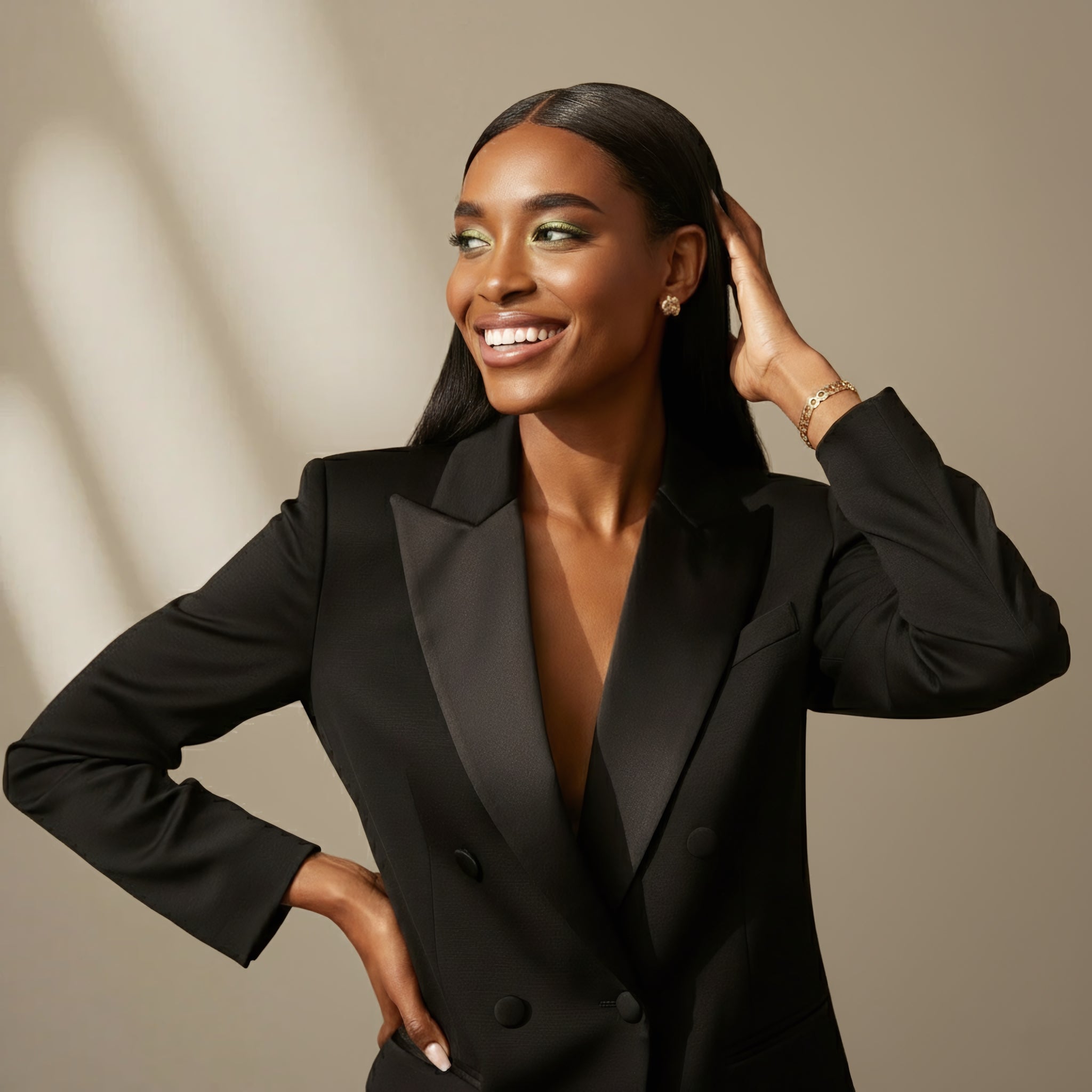 A woman in a tailored black blazer smiles and touches her sleek, straight hair beneath warm sunlight against a pale textured wall. An elegant lifestyle portrait for Allnord’s HYGÉE La Chevelure with luminous, healthy‑hair styling and refined minimalism.