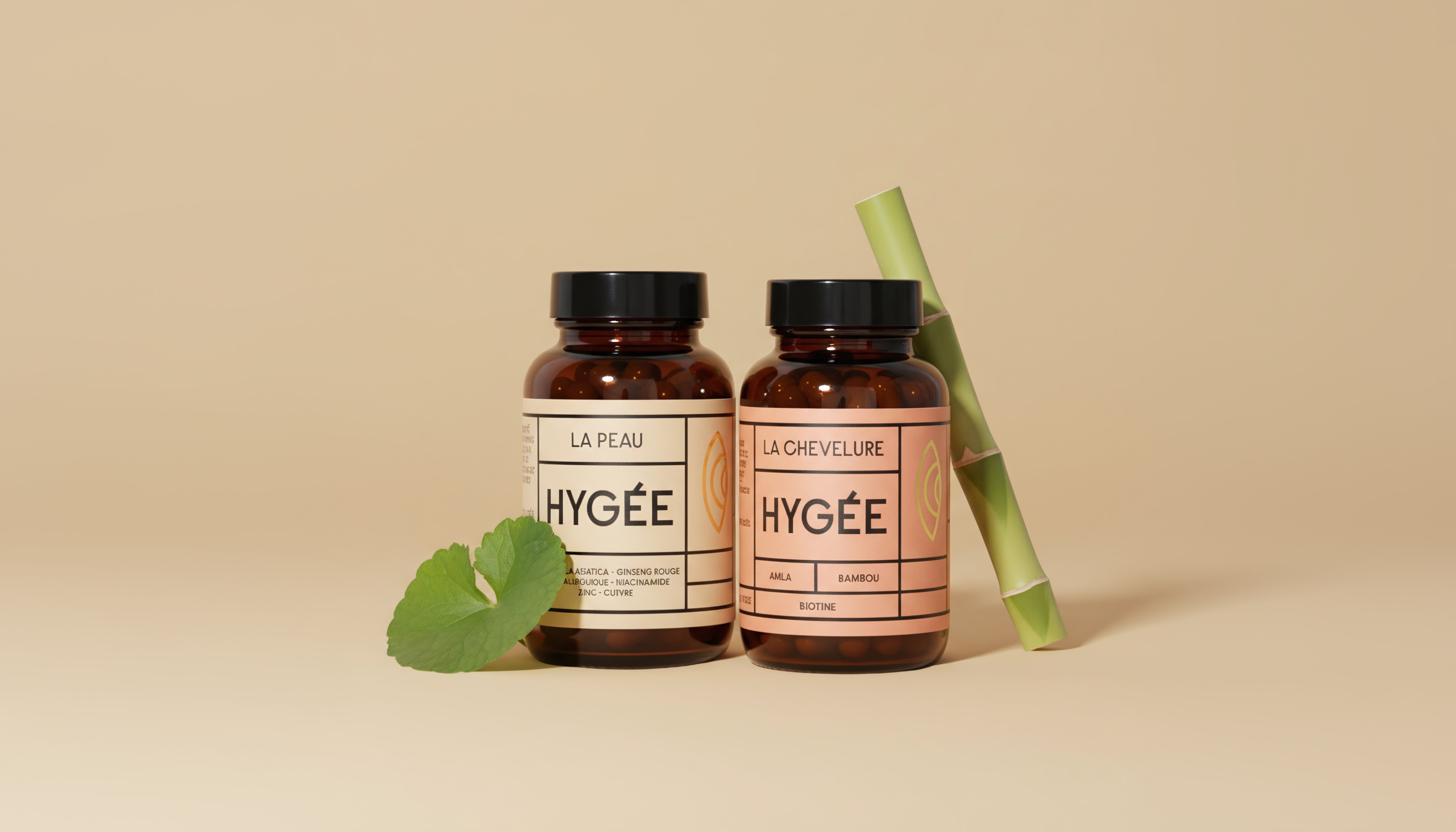 Two amber HYGÉE bottles, La Peau and La Chevelure, stand side by side on a beige background styled with a fresh green centella leaf and upright bamboo stems.
