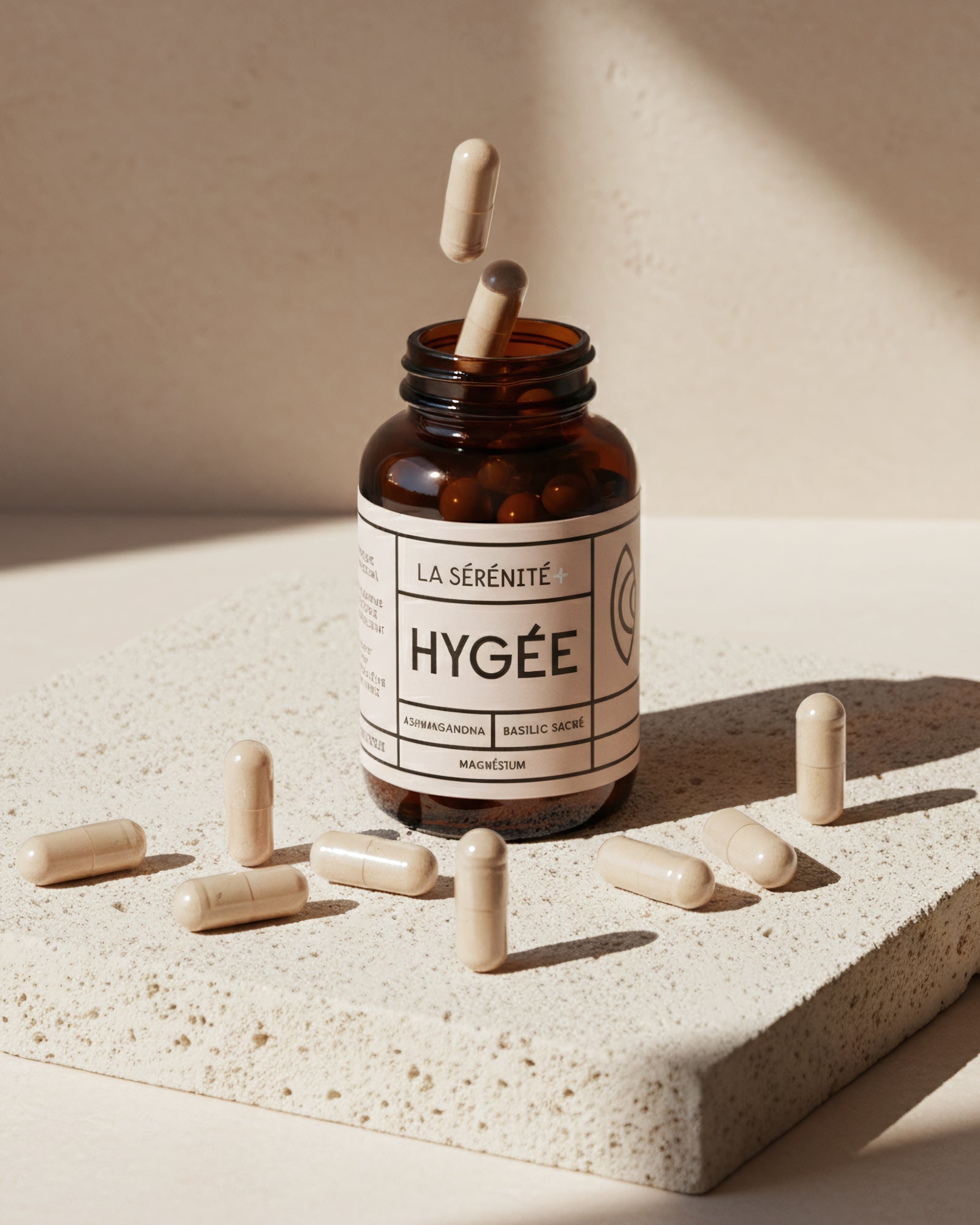 An amber HYGÉE La Sérénité+ bottle sits on a textured stone slab with beige capsules scattered around and two capsules floating above the open neck in bright sun.​